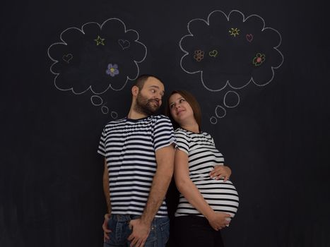 portrait of husband and pregnant wife posing against black chalk drawing board