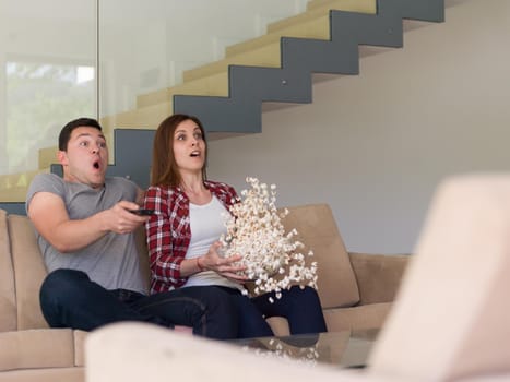 young handsome couple enjoying free time watching television with popcorn in their luxury home villa