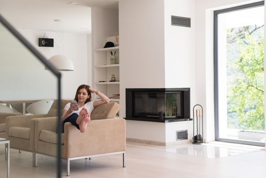 young happy woman sitting on sofa with mobile phone at luxury home