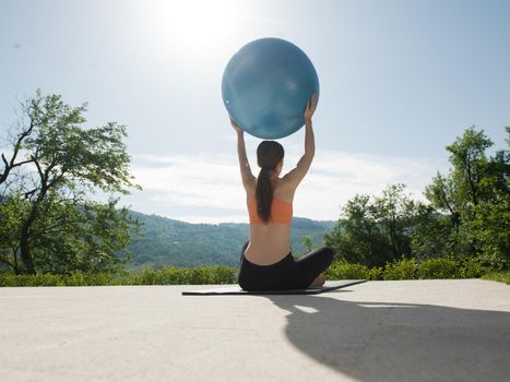 young beautiful woman doing exercise with pilates ball in front of her luxury home villa