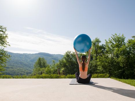 young beautiful woman doing exercise with pilates ball in front of her luxury home villa