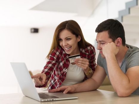 happy young couple buying online using laptop a computer and a credit card in their luxury home villa