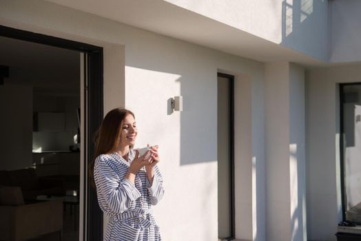 young beautiful woman in a bathrobe enjoying morning coffee in front of her luxury home villa