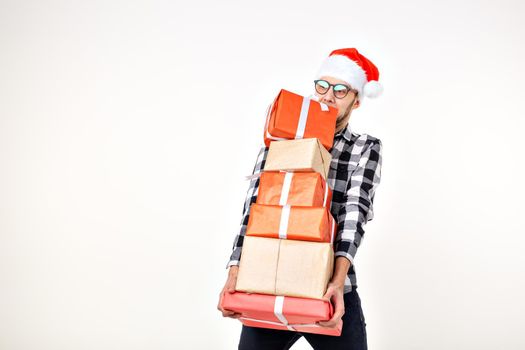 Holidays and presents concept - Funny man in Christmas hat holding many gift boxes on white background.