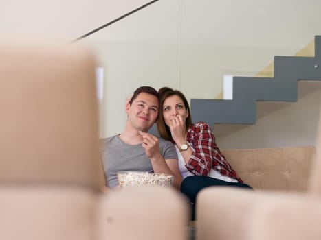 young handsome couple enjoying free time watching television with popcorn in their luxury home villa