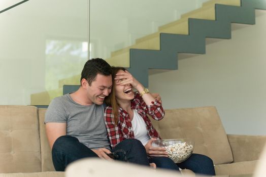 young handsome couple enjoying free time watching television with popcorn in their luxury home villa