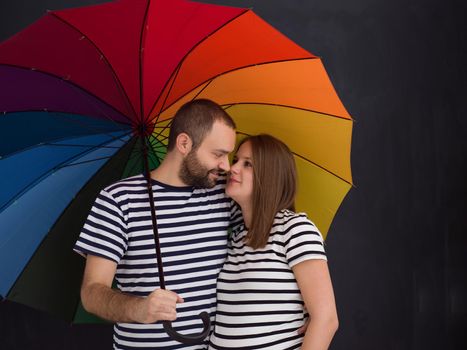 portrait of husband and pregnant wife posing with colorful umbrella in front of black chalk drawing board