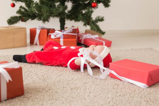 Beautiful little baby celebrates Christmas. New Year's holidays. Baby in a Christmas costume and in santa hat and gift box.