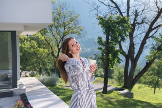 young beautiful woman in a bathrobe enjoying morning coffee in front of her luxury home villa