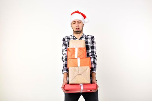 Holidays and presents concept - Funny man in Christmas hat holding many gift boxes on white background.