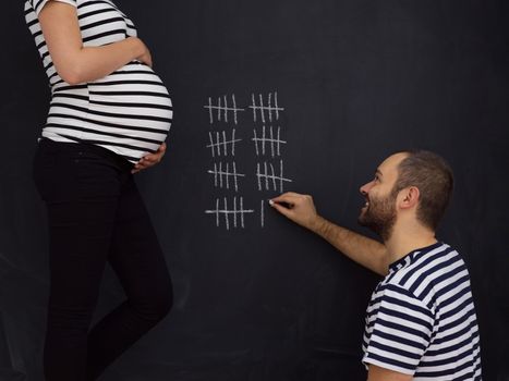 young pregnant couple accounts week of pregnancy and writing them with chalk on blackboard