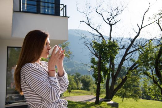 young beautiful woman in a bathrobe enjoying morning coffee in front of her luxury home villa