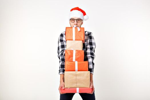 Holidays and presents concept - Funny man in Christmas hat holding many gift boxes on white background.