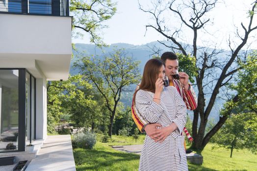 Young beautiful couple in bathrobes are enjoying morning coffee in front of their luxury home villa