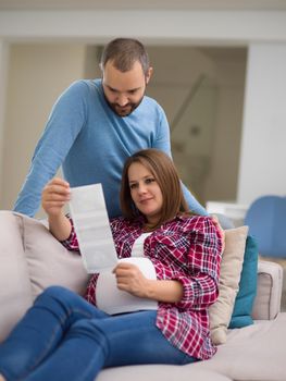 Young pregnant couple looking baby's ultrasound photo while relaxing on sofa at home