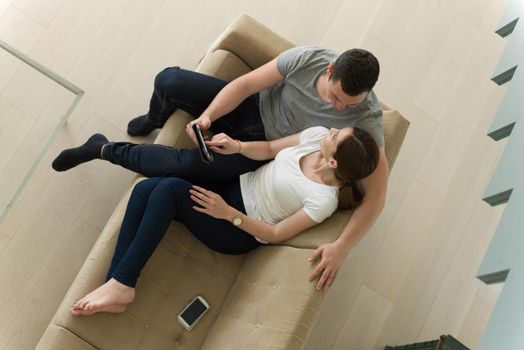 Young couple relaxing at luxurious home with tablet computers reading in the living room on the sofa couch.