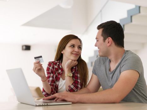 happy young couple buying online using laptop a computer and a credit card in their luxury home villa