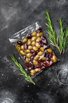 Green and black olives in pack set, on black dark stone table background, top view flat lay, with copy space for text