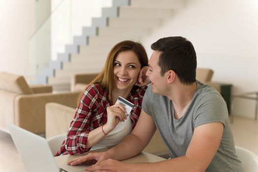 happy young couple buying online using laptop a computer and a credit card in their luxury home villa