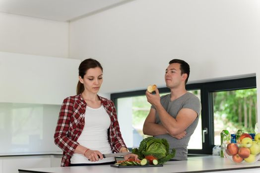 Young handsome couple in the kitchen  beautiful woman preparing a salad while the man eating an apple