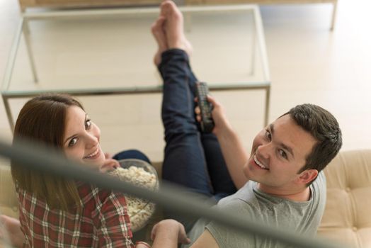 young handsome couple enjoying free time watching television with popcorn in their luxury home villa