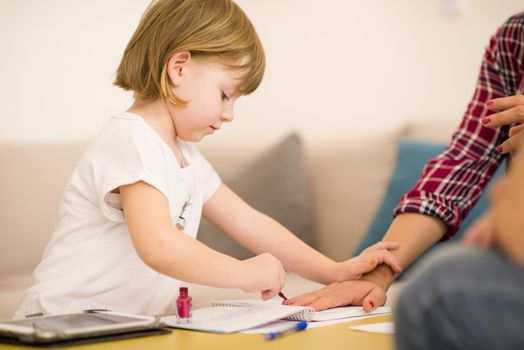 little cute daughter painting nails to her pregnant mom while relaxing at home