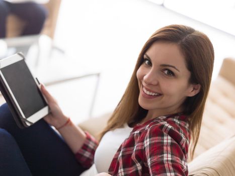 Young couple relaxing at luxurious home with tablet and laptop computers reading in the living room on the sofa couch.