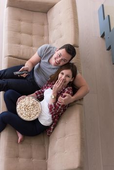 young handsome couple enjoying free time watching television with popcorn in their luxury home villa