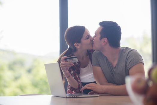 happy young couple buying online using laptop a computer and a credit card in their luxury home villa