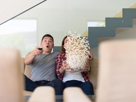 young handsome couple enjoying free time watching television with popcorn in their luxury home villa