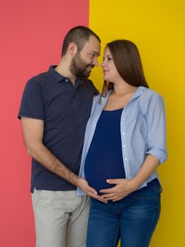 Portrait of a happy young couple,man holding his pregnant wife belly isolated over colorful background