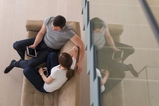 Young couple relaxing at luxurious home with tablet computers reading in the living room on the sofa couch.