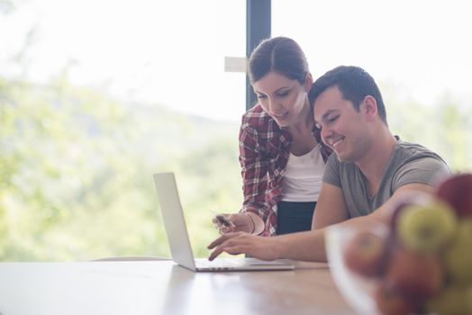 happy young couple buying online using laptop a computer and a credit card in their luxury home villa