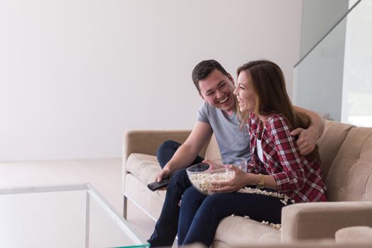 young handsome couple enjoying free time watching television with popcorn in their luxury home villa