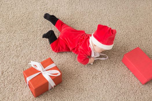 Beautiful little baby celebrates Christmas. New Year's holidays. Baby in a Christmas costume and in santa hat and gift box, top view.