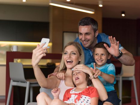 Happy family siting on sofa and using cell phone for video call  at home