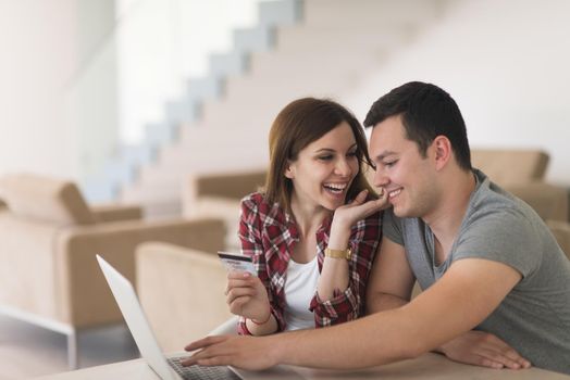 happy young couple buying online using laptop a computer and a credit card in their luxury home villa