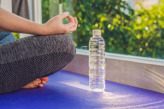 hand of a woman meditating in a yoga pose on a rug for yoga and a bottle of water.