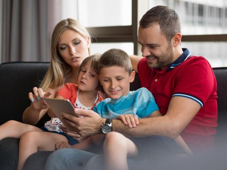 Happy Young Family Playing Together with tablet at home sitting on the sofa