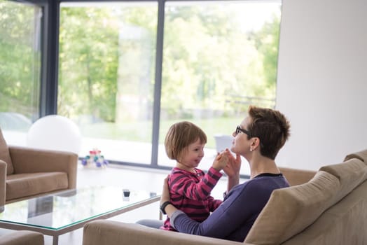 young mother and cute little girl enjoying their free time hugging on the sofa in their luxury home villa