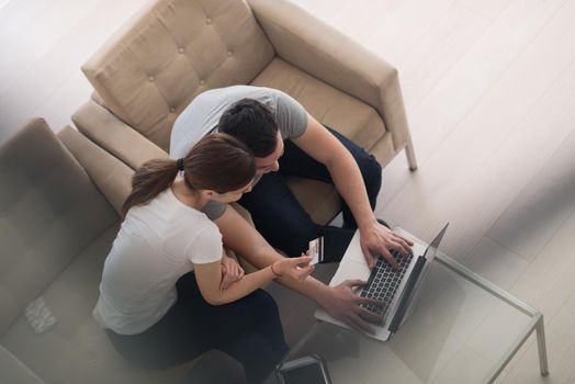 happy young couple buying online using laptop a computer and a credit card in their luxury home villa