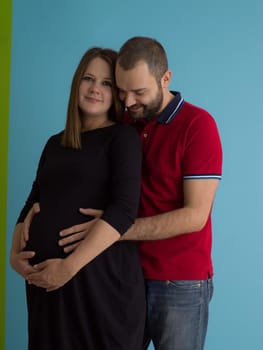 Portrait of a happy young couple,man holding his pregnant wife belly isolated over blue background