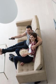 young handsome couple enjoying free time watching television with popcorn in their luxury home villa