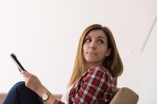 young happy woman sitting on sofa with tablet computer at luxury home