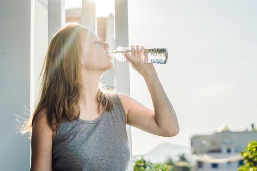 Young woman is drinking water on the sunset background.