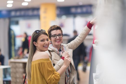 Two Girl-Friends On Shopping Walk On Shopping Centre With Bags And Choosing