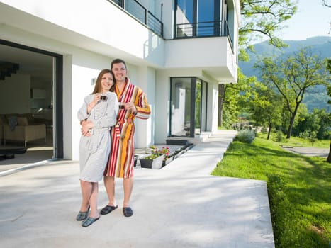 Young beautiful couple in bathrobes are enjoying morning coffee in front of their luxury home villa