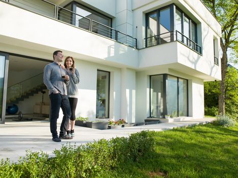 young beautiful handsome couple enjoying morning coffee in front of their luxury home villa