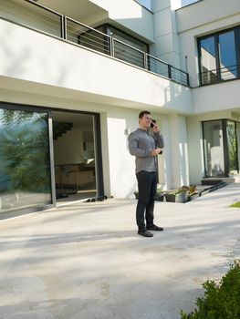 young handsome successful man using mobile phone in front of his luxury home villa