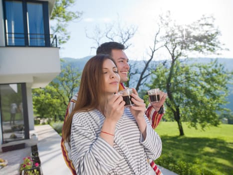 Young beautiful couple in bathrobes are enjoying morning coffee in front of their luxury home villa